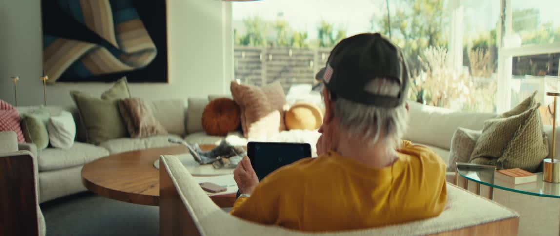 A man is sitting in a living room holding a tablet