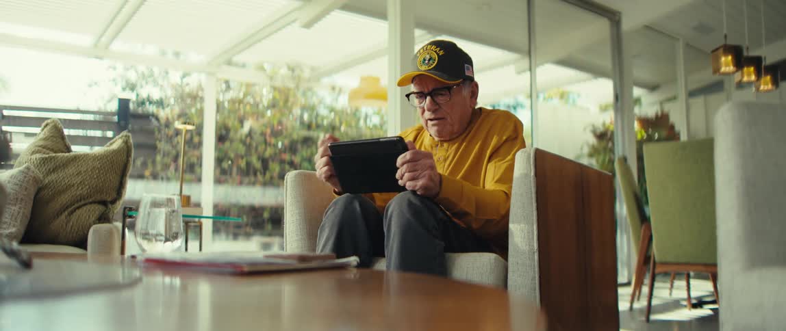 Man sitting at home cheers while viewing his tablet during the daytime