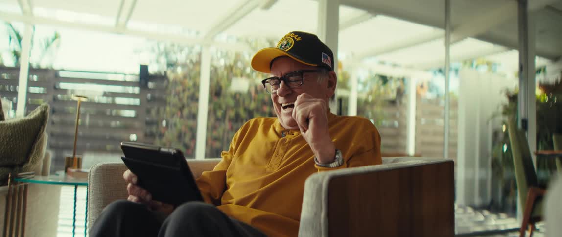 Man sitting on a couch holding a tablet computer bursting into laughter