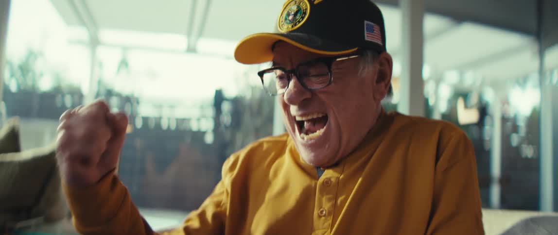 Elderly man cheers while viewing media on his computer at home during the daytime