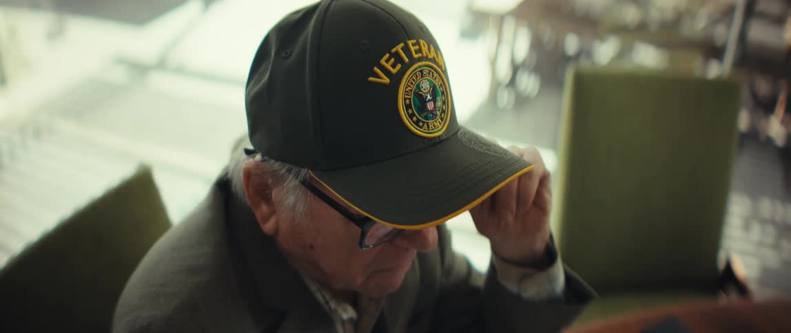 An elderly man sits in a sunlight room in deep thought as he removes his eyeglasses