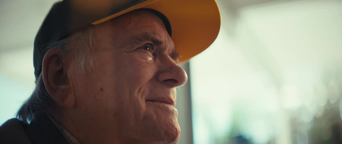 Elderly man wearing a cap looking ahead with a slight smile in a welllit indoor setting