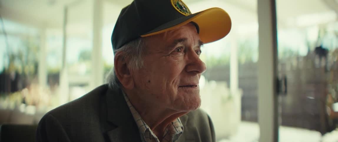 An elderly man sits in a sunlit modern living room smiling and looking ahead