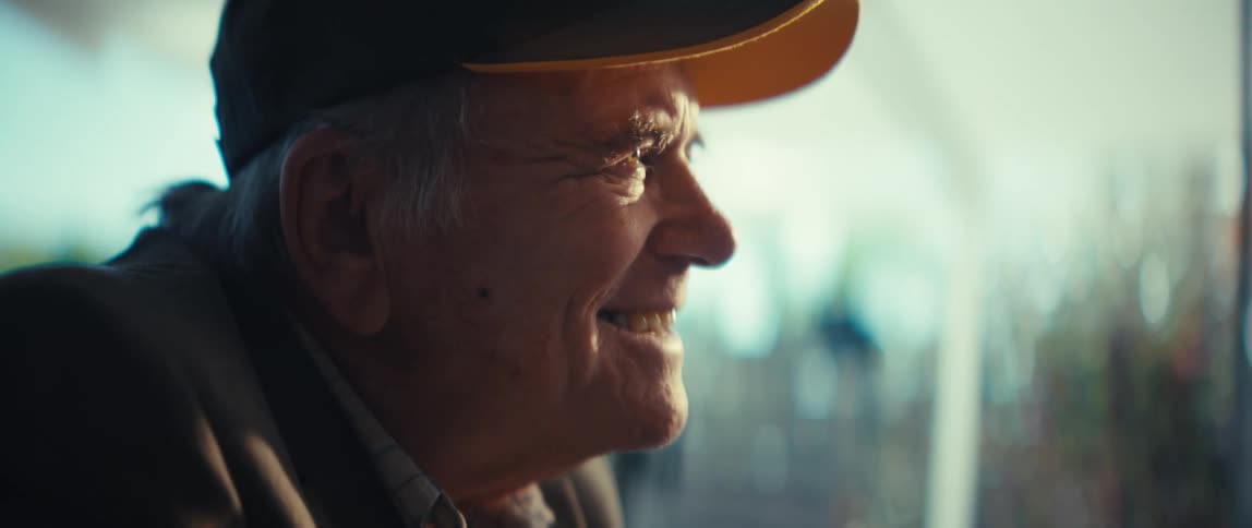 Elderly man wearing a cap smiles in profile in a welllit indoor setting