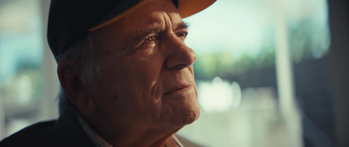 Elderly man wearing a cap with a serious expression in a welllit indoor setting