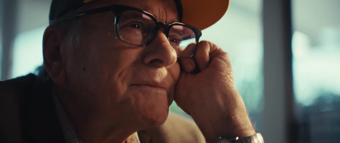 An elderly man wearing glasses fights back tears while his lips tremble