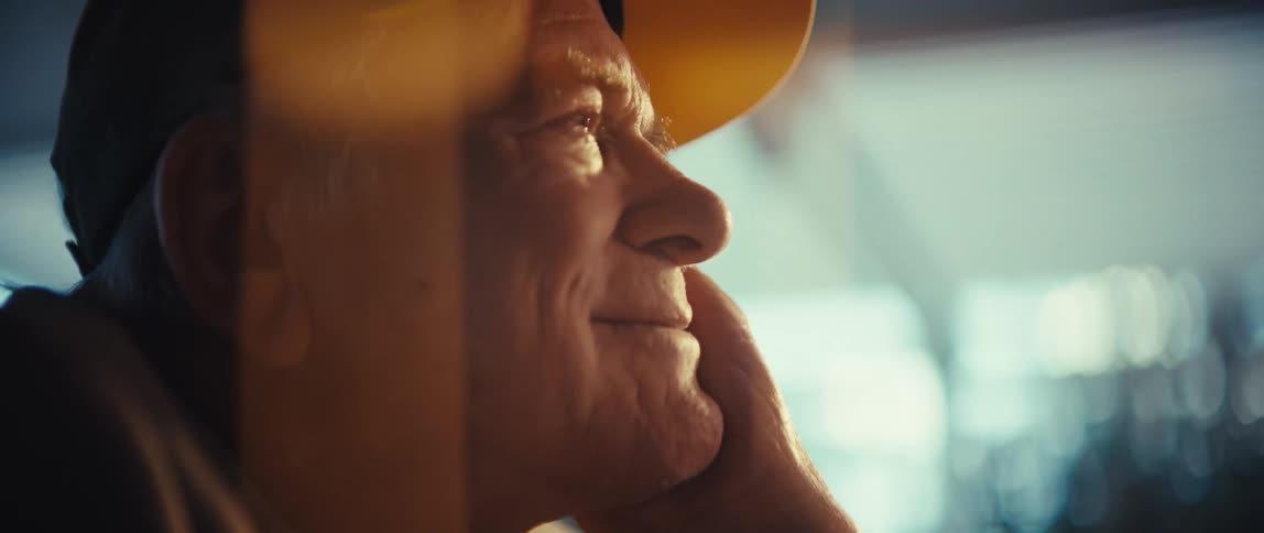 Elderly man wearing a baseball cap smiling with a contemplative facial expression indoors during day time