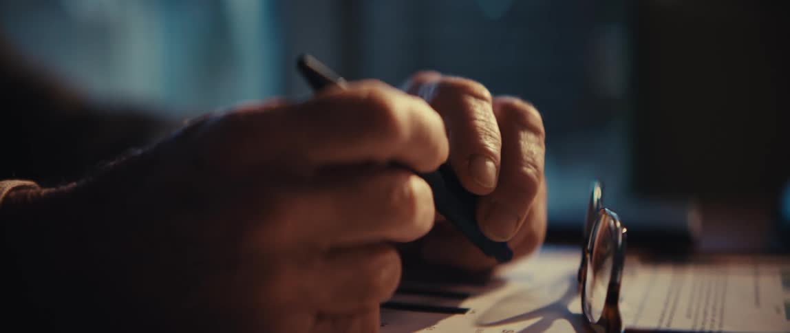 Hands holding a pen on a table with glasses placed beside