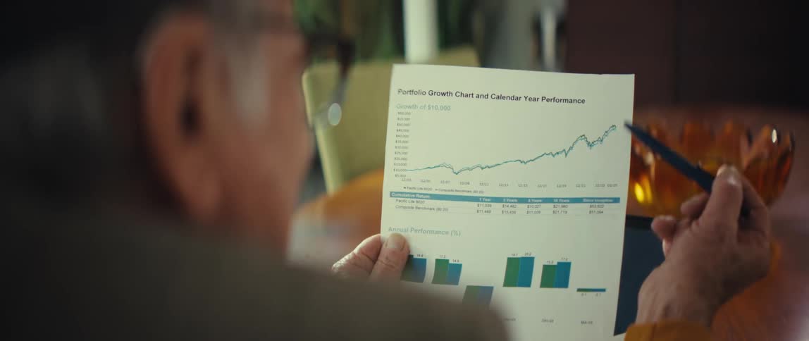 Man holding a printed report with a financial growth chart while pointing to an upward line with a pen