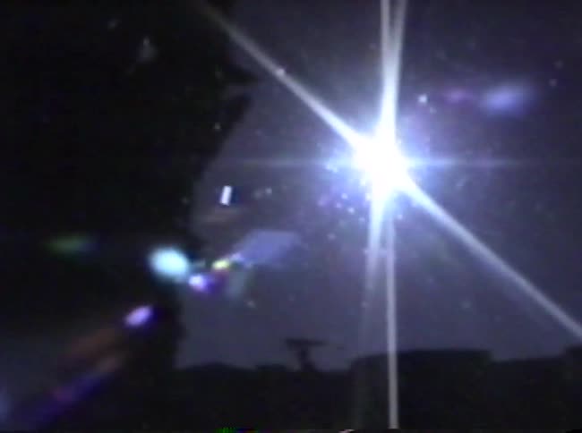 A vintage video shows a tree and then pans to a bright sun with strong lens flare against a blue sky with dark silhouettes of a distant landscape