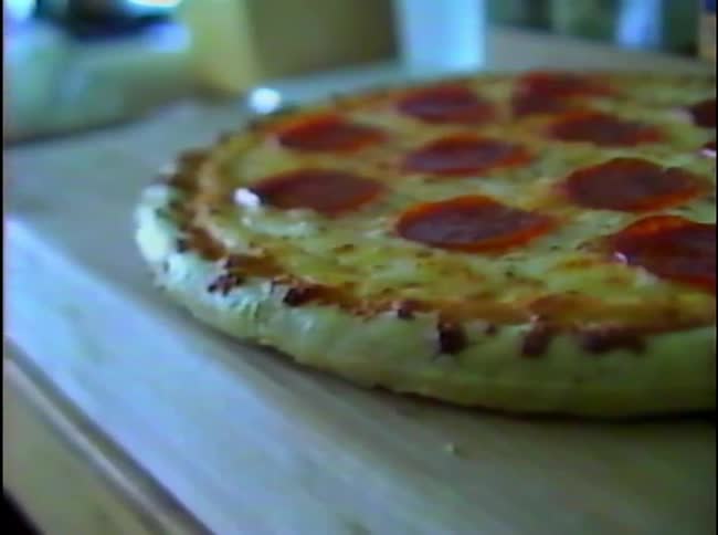 A whole pepperoni pizza with melted cheese sits on a wooden board in a kitchen during a close view