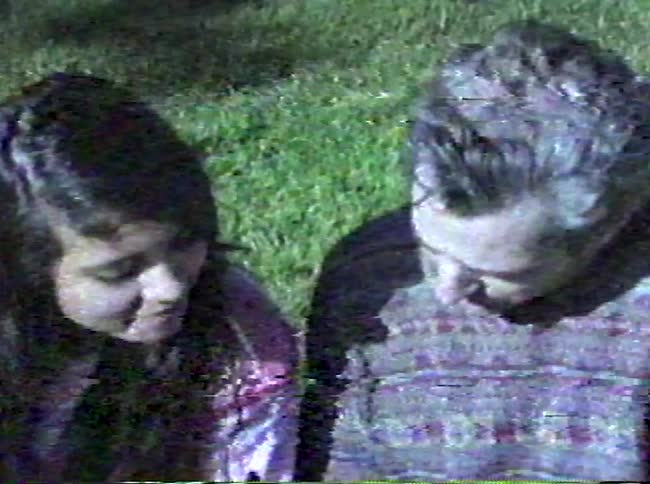 A young woman and an older man sit on the grass together looking at a notebook and talkingthe woman smiles as she watches the man write or draw in the notebook appearing to enjoy their time together