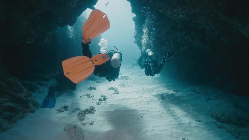 Divers with tanks explore an underwater passage between rock formations