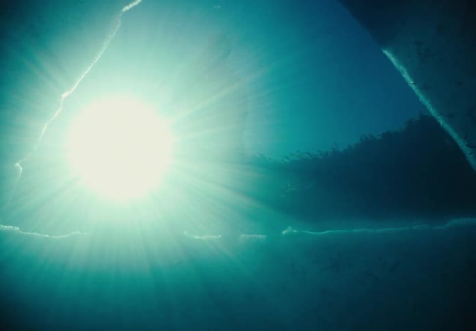 Under water shot of Light shines past a person onto the reflective water in a break in the ice at night