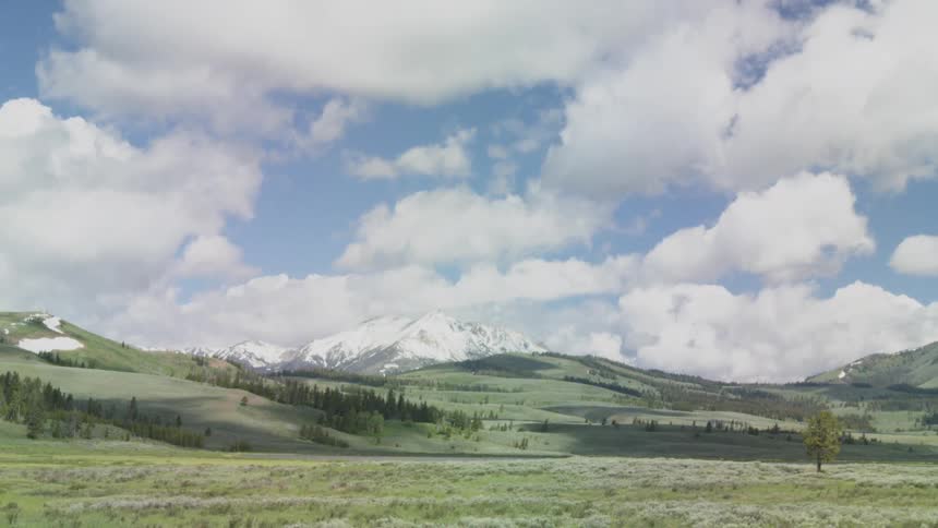 Cumulus clouds passing overhead cast shadows on the hills and grassland located while snow cover covers the mountain in the background