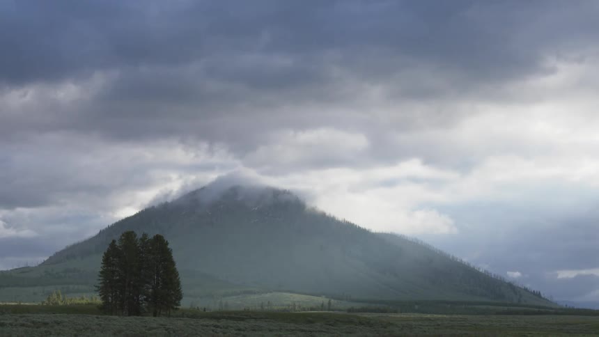 Heavy clouds over a mountain next to a field outdoors during day time