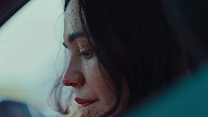 A woman with long dark hair looks out of a car window while sitting in the passenger seat