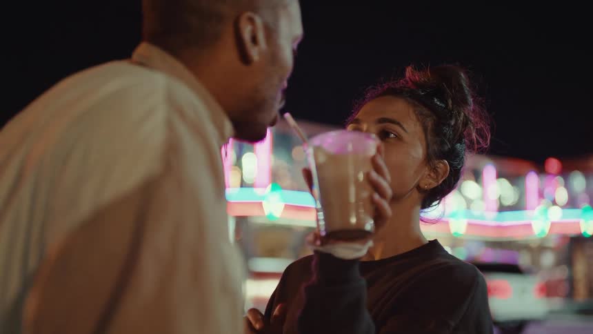 A woman is sharing her drink with a man in the parking lot of a restaurant