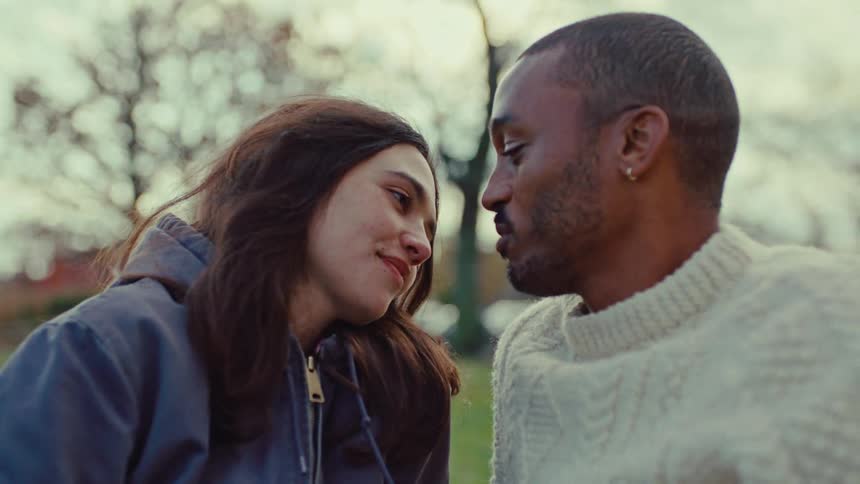 Couple in the park smiles and talks while sitting close together on an autumn day