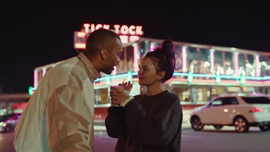 A woman is sharing her drink dessert with a man outside a restaurant