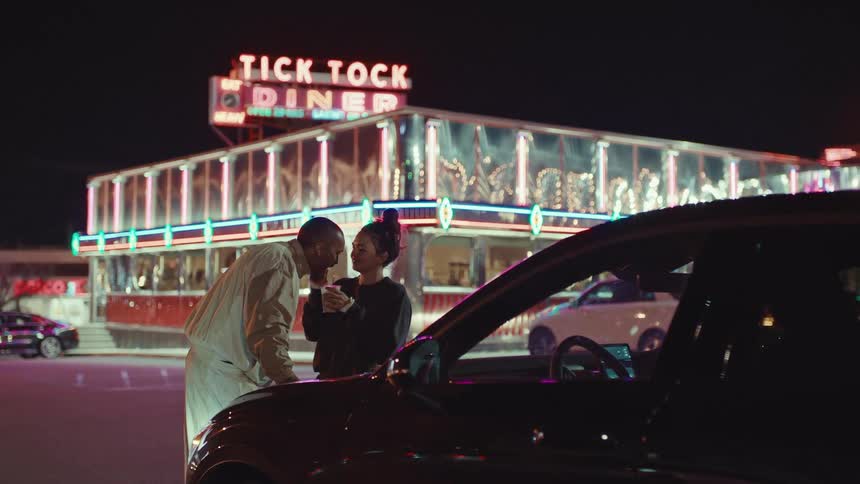Couple beside a car in front of a diner with a neon sign at night