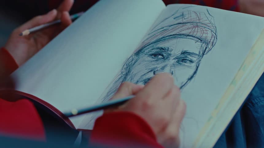 A sketch artist using a pen to draw a mans face on a white sheet of paper