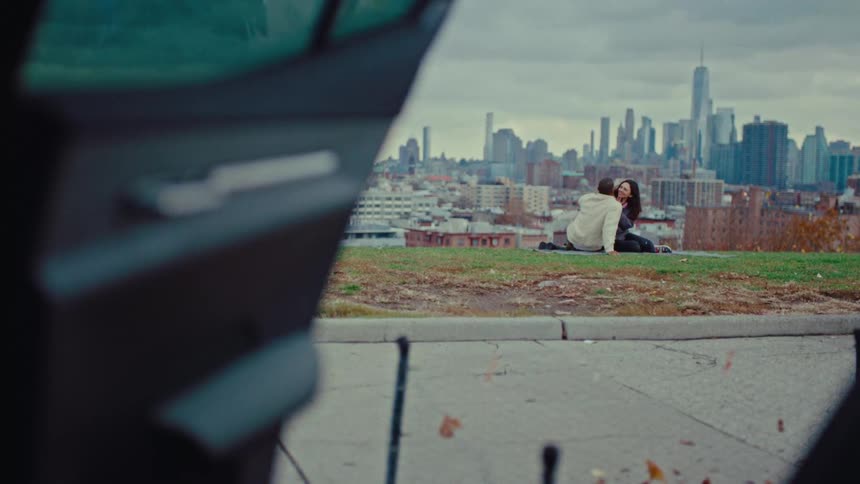 Couple sitting on the grass in a park with skyscrapers in the background