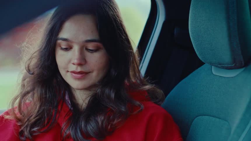 A young woman is sitting slightly to the side in a vehicle smiling and looking to her side