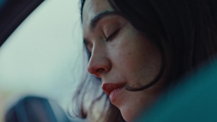 A closeup of a womans face inside a car her expression pensive as she gazes forward