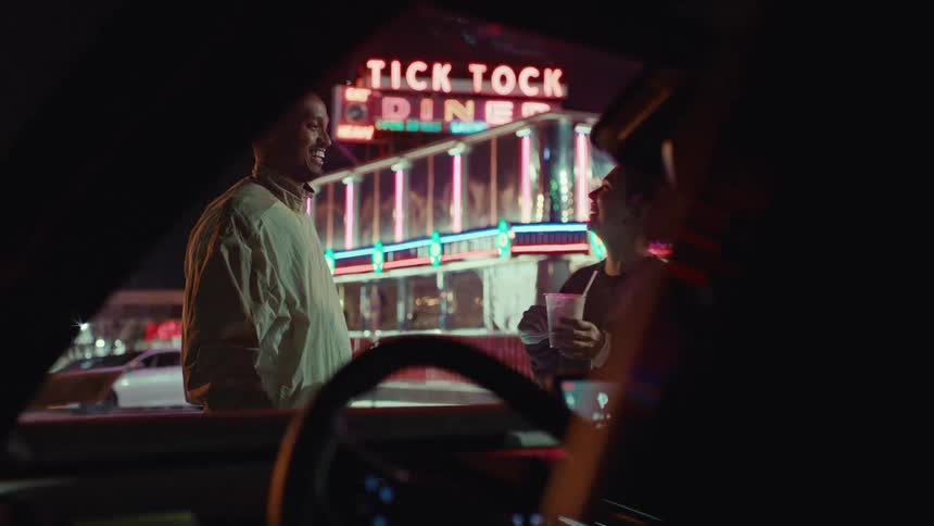 Couple kissing in front of a diner illuminated by a neon sign at night