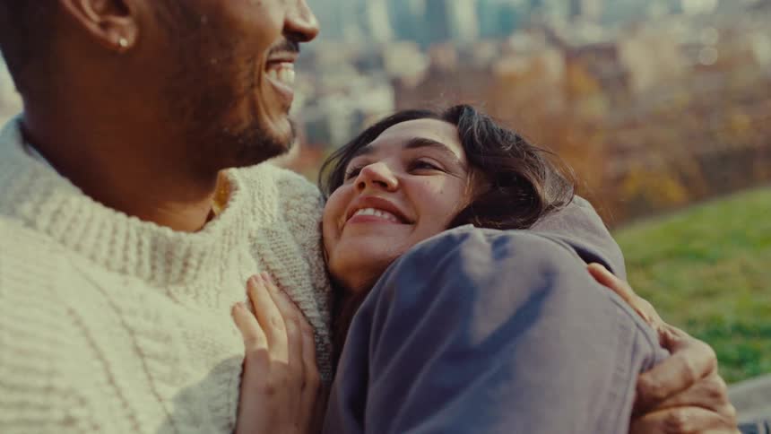 Smiling couple talks together while cuddling in a park outside the city on an autumn day