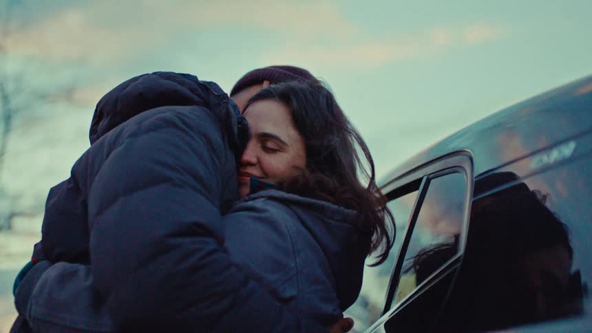A couple are standing and hugging each other next to a vehicle outdoors