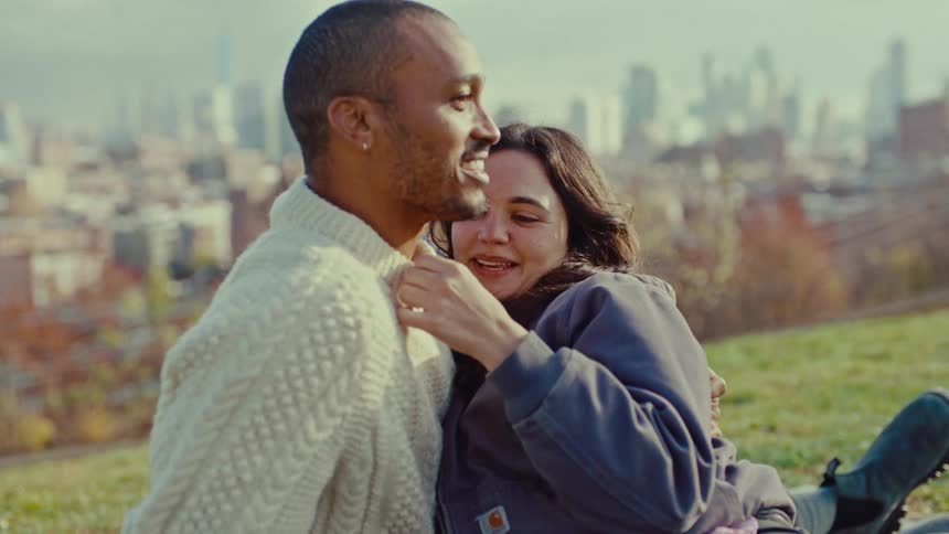 A woman romantically touches a mans chest while they sit outdoors on an autumn day