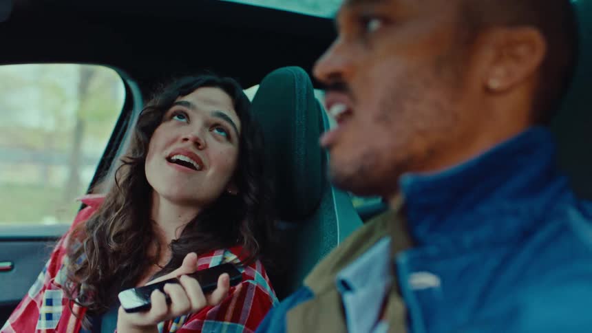 A man driving and his female passenger are singing in the car