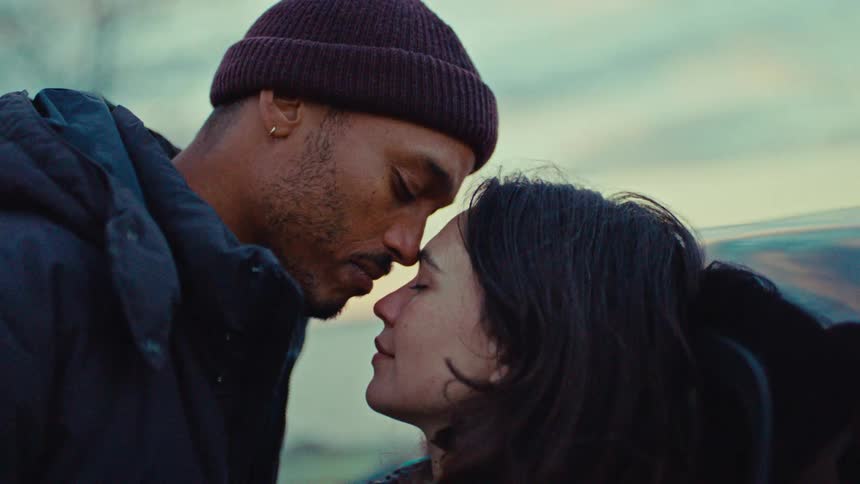 Young adult couple nuzzling romantically against a car outdoors during day time