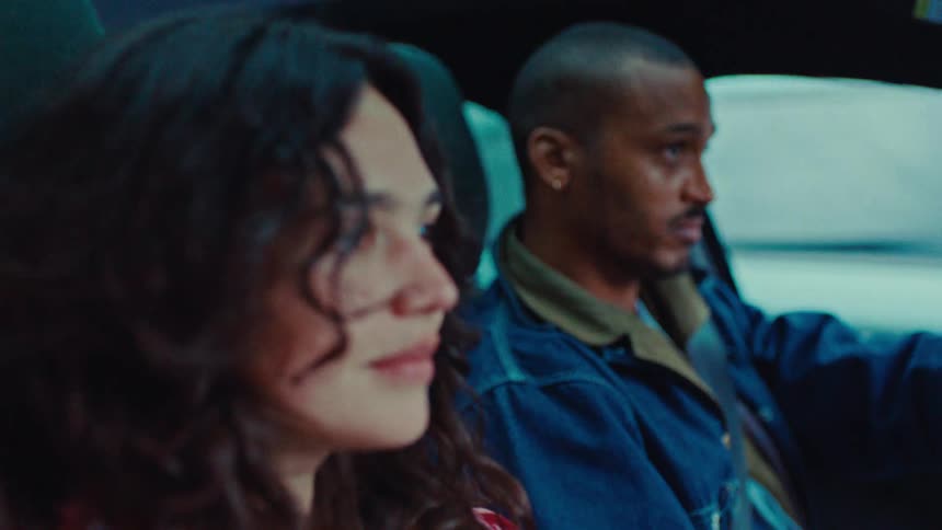 Young adult woman sitting on the passenger seat of a vehicle and talking to a young adult black man driving during day time