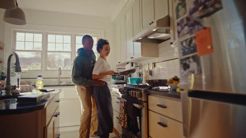 Man hugging a woman while she cooks at the stove