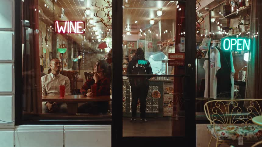 Couple talking at a table inside a restaurant with neon signs on the facade