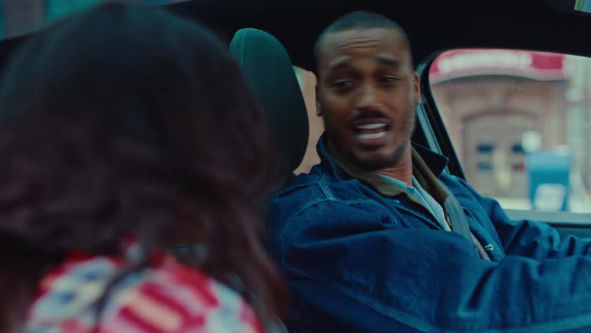 A young man and a young woman sitting inside a car having fun as they sing and nod along to a song playing from the car stereo