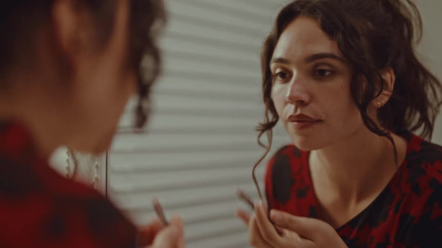 The woman is putting on lipstick in the mirror