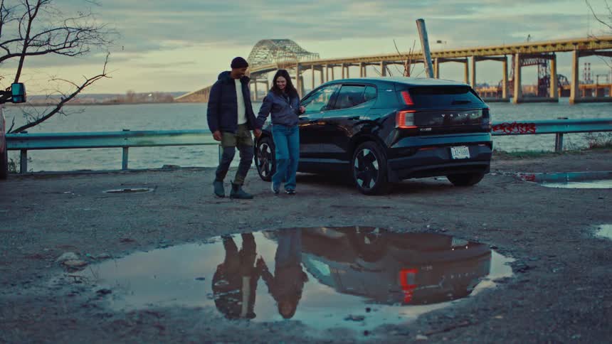 Couple dances in a waterside parking lot containing reflective puddles on a winter day