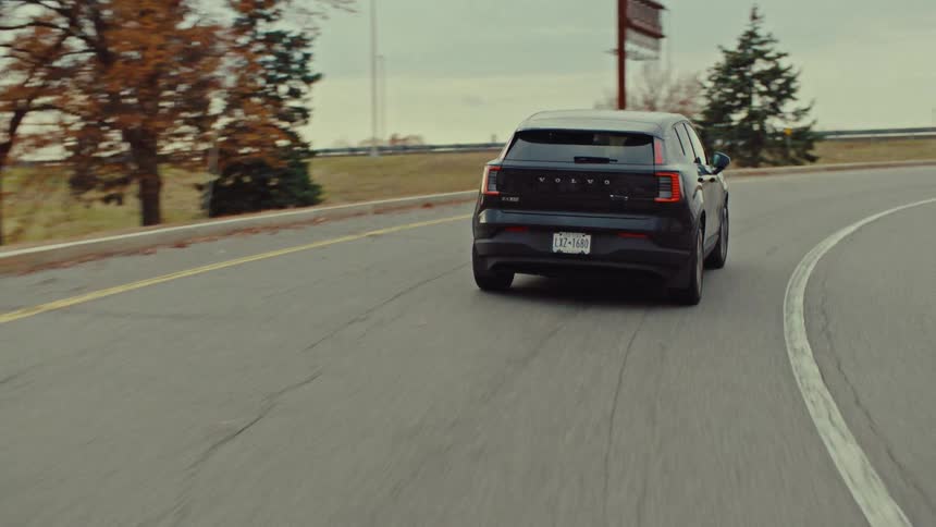 A dark colored car is driving a long a road that leads to a highway