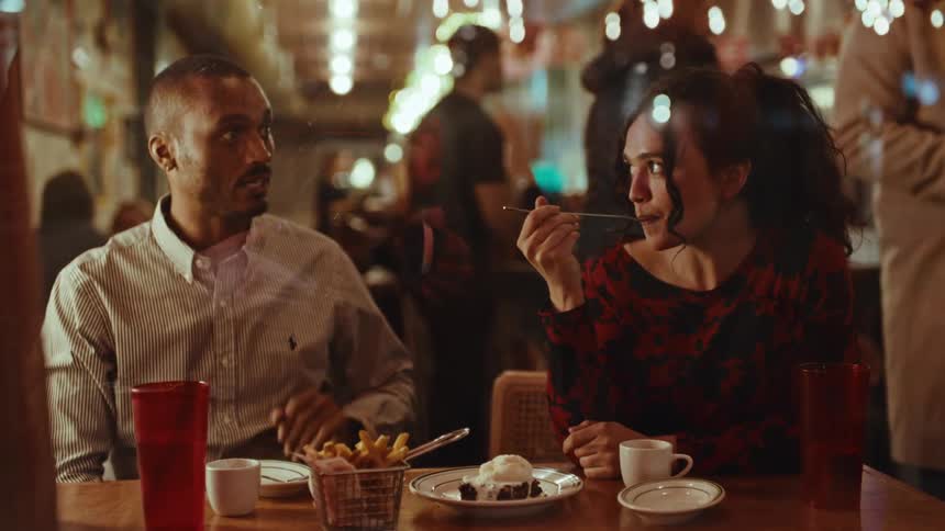 Woman holding a spoon with dessert while talking to a man at a table in a restaurant
