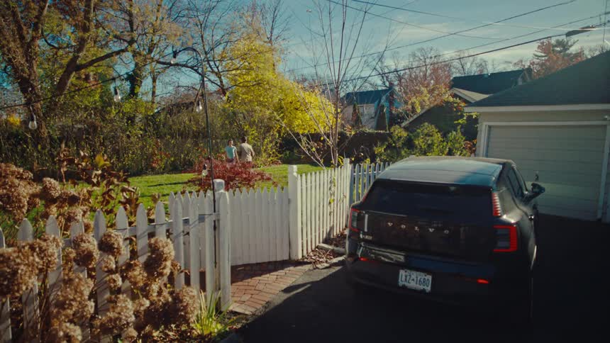 Two people are playing catch with a football in a backyard next to a car parked in a driveway