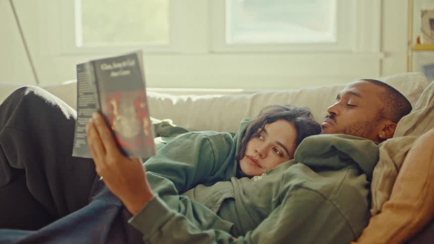 Man reading a book on the couch while a woman rests her head on his chest