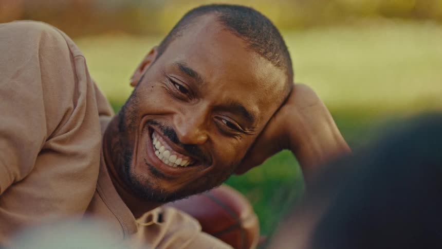 Man smiling while resting his head on his arm outdoors