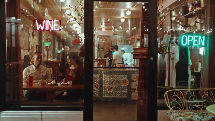 A man and woman sit at a table inside of a small restaurant