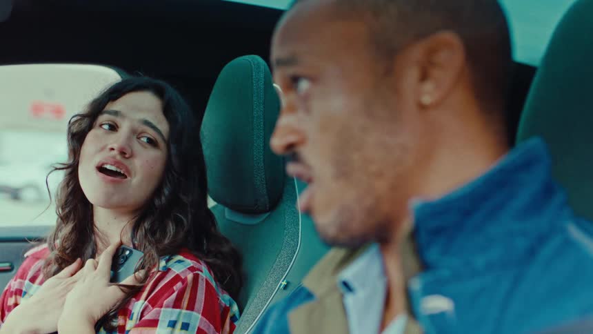 A man and young woman are seated singing happily in a vehicle while it is traveling through a city