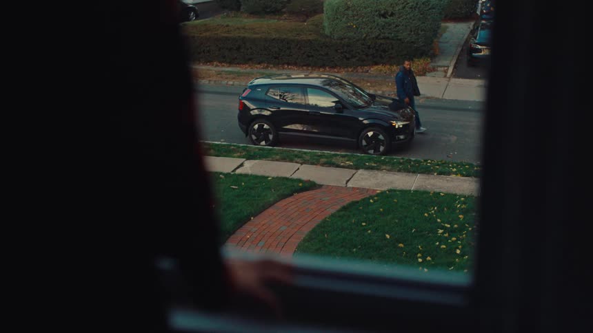 Person looking out of an upstairs window as a man gets out of an automobile parked on the street