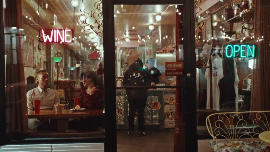 Couple sitting at a table inside a restaurant with neon signs on the facade